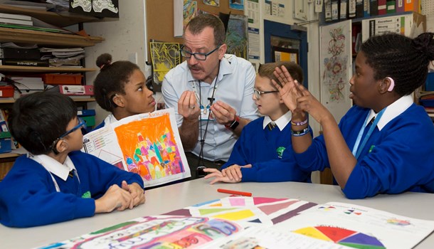 A teacher signs to four deaf pupils at a project table.