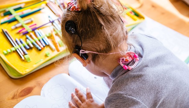 A girl wearing a cochlear implant colours in a colouring book. 