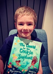 Young boy holding a copy of The Quest for the Cockle Implant