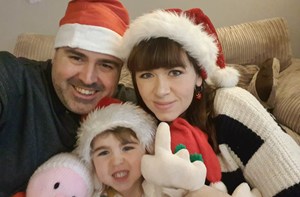 Mum and dad sitting on the sofa with a little girl, all wearing Christmas hats