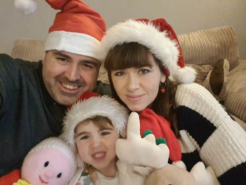 Mum and dad sitting on the sofa with a little girl, all wearing Christmas hats