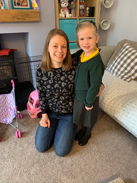 Mum kneeling on the floor next to little girl in green and yellow school uniform