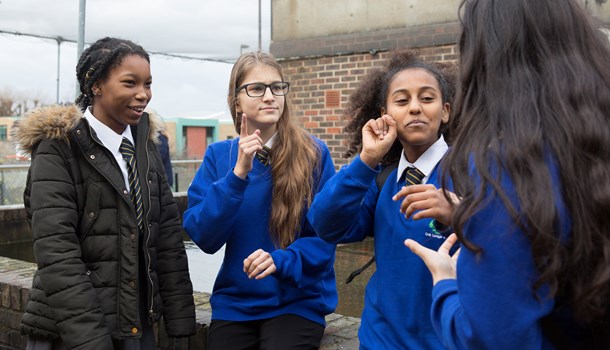 Four deaf teenage girls in school uniforms sign to each other. 