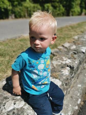 Young blonde boy with hearing aids sitting outside on a wall