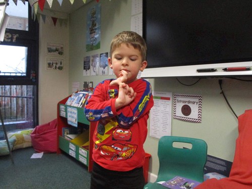 Young boy standing in a classroom doing BSL signs