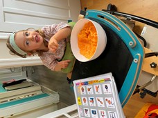 Little girl sat in a supported wheelchair with a tray in front of her holding a baking bowl