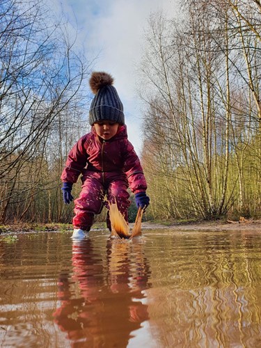 Little girl in a snow suit and woolly hat splashing in a puddle