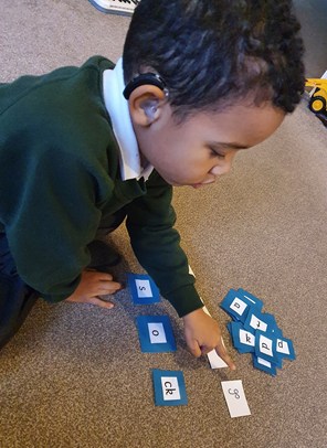 Photo of a little boy in school uniform playing on the carpet with letter cards