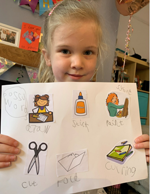 Little girl with blonde hair holding a poster she's made with cut out pictures stuck on