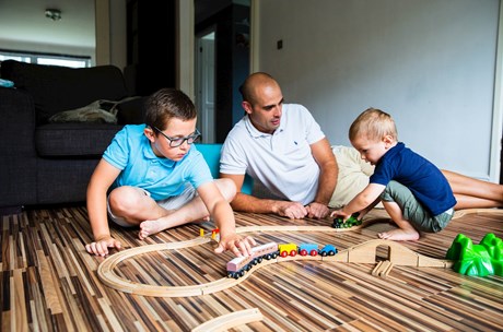 Two sons sitting on the floor with their dad, playing with a wooden model railway set