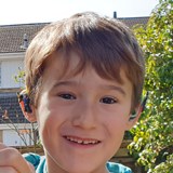 Photo of a young boy wearing a blue tshirt smiling at the camera