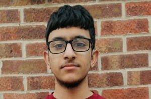 Photo of a teenage boy wearing a red jumper standing against a brick wall holding a certificate