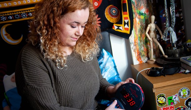 A young woman with curly hair presses a button on a Sonic Boom alarm clock.