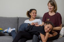 Mother and two daughters sitting on the sofa smiling.