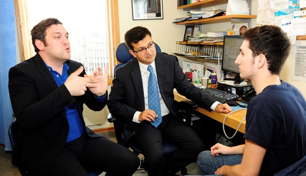 A young man sits in a doctor's office facing the doctor and an interpreter. 