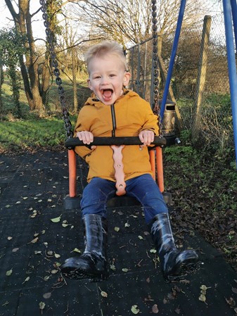 Photo shows a young boy wearing a yellow jacket on a swing smiling