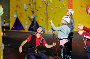 Climbing instructor helping two deaf children hold onto climbing ropes at an indoor climbing centre.