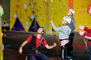 Climbing instructor helping two deaf children hold onto climbing ropes at an indoor climbing centre. 
