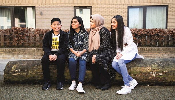 Hamza sitting on a log outside with his mum and two sisters.