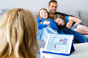 A parent looks at an ipad, on a table in front of their family.