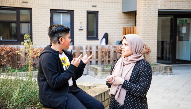 A boy wearing a cochlear implant signs to a woman wearing a hijab.