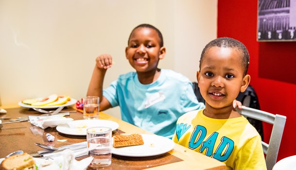 Two brothers sit at a table eating breakfast and smiling at the camera.