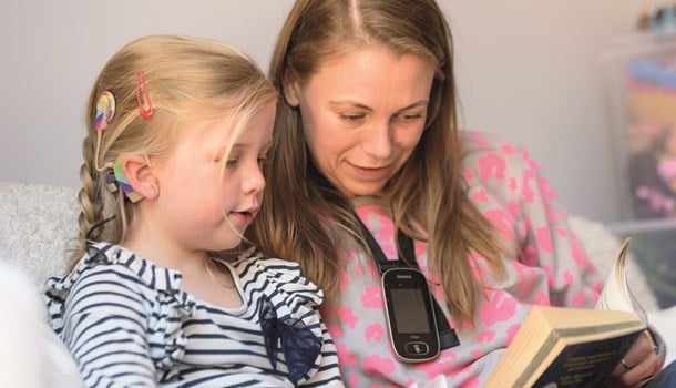 A young girl with a cochlear implant reading with her mum who's wearing a radio aid.