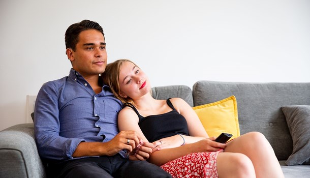 Two teenagers sit on the sofa, the girl resting her head on her boyfriend's shoulder.