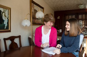 A teenager and her mum look at paperwork together at their dining table.