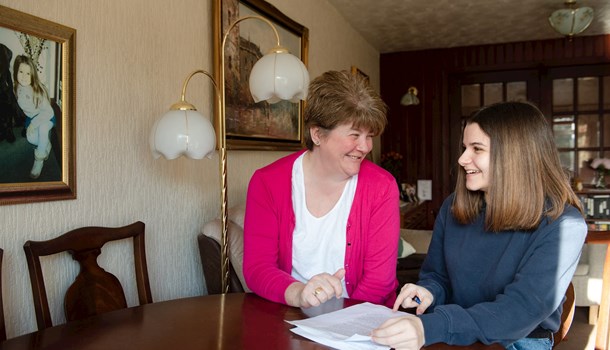 A teenager and her mum look at paperwork together at their dining table.