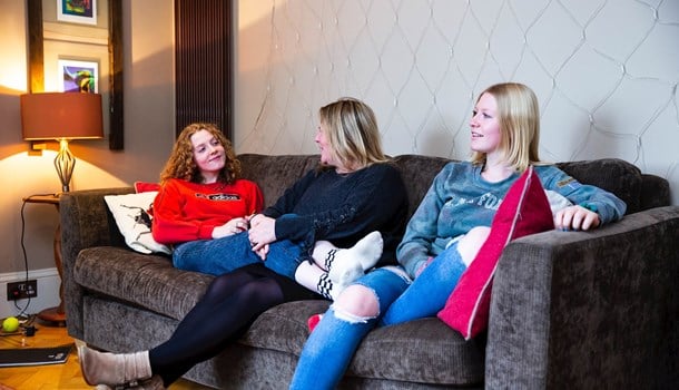 A mum and her two teenage daughters relax together on the sofa.