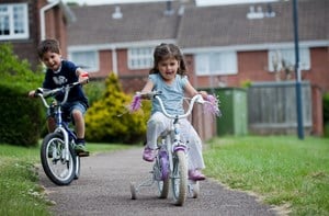 Two small children bike on a paved path.