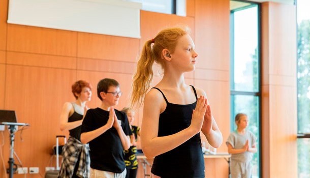 A child with a hearing aid practices dance in a studio with others.