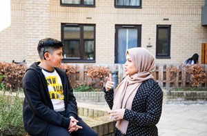 A woman in a hijab signing to a deaf young boy sitting on a wall