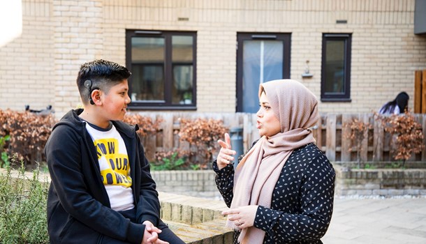 A woman in a hijab signing to a deaf young boy sitting on a wall