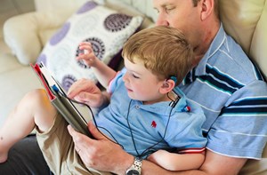 A deaf child with a hearing aid and a his dad watching a tablet together