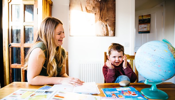 A mum and her son sit at an activity table laughing.