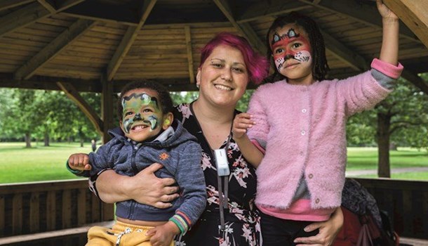Mum Chrysanthi holds her two children who have face paint on in a gazebo.