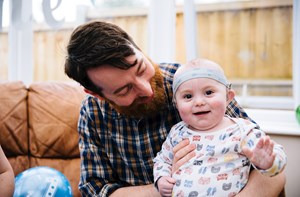 A deaf baby with cochlear implants on their dad's knee