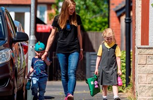 Young girl with cochlear implants walking to school with mum and brother