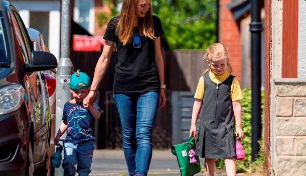 Young girl with cochlear implants walking to school with mum and brother.