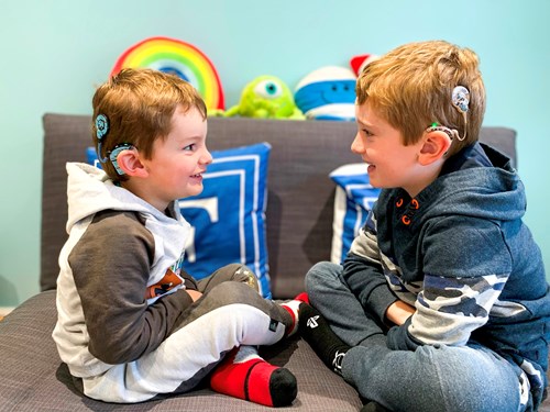Boys sitting facing each other with cochlear implants on.