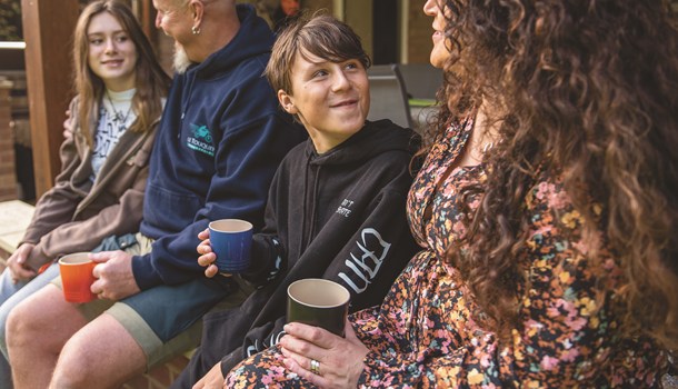 A teenage boy drinks a warm drink outside with his family.