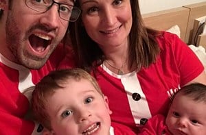 A mum and dad hold their young son and newborn while wearing Christmas shirts