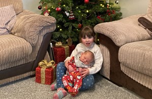 Young girl holds her baby brother by a Christmas tree