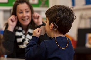 An early years practitioner interacting with a young deaf boy in a classroom.