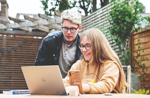 Two people look at a laptop on a table in a garden.