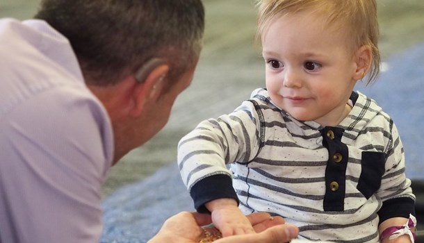 Deaf baby playing and smiling at man with hearing aid
