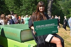 Young woman at graduation holding a sign that read 'Stirling Graduate - Be the Difference'