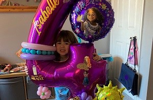 Isabelle (4) smiling behind a giant balloon in the shape of a 4